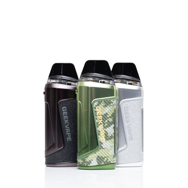 Three GEEKVAPE pod mod vape devices standing side by side on a white reflective surface. The left device is dark metallic gray/black, the center device has a green camouflage pattern with gold lettering, and the right device is metallic silver.